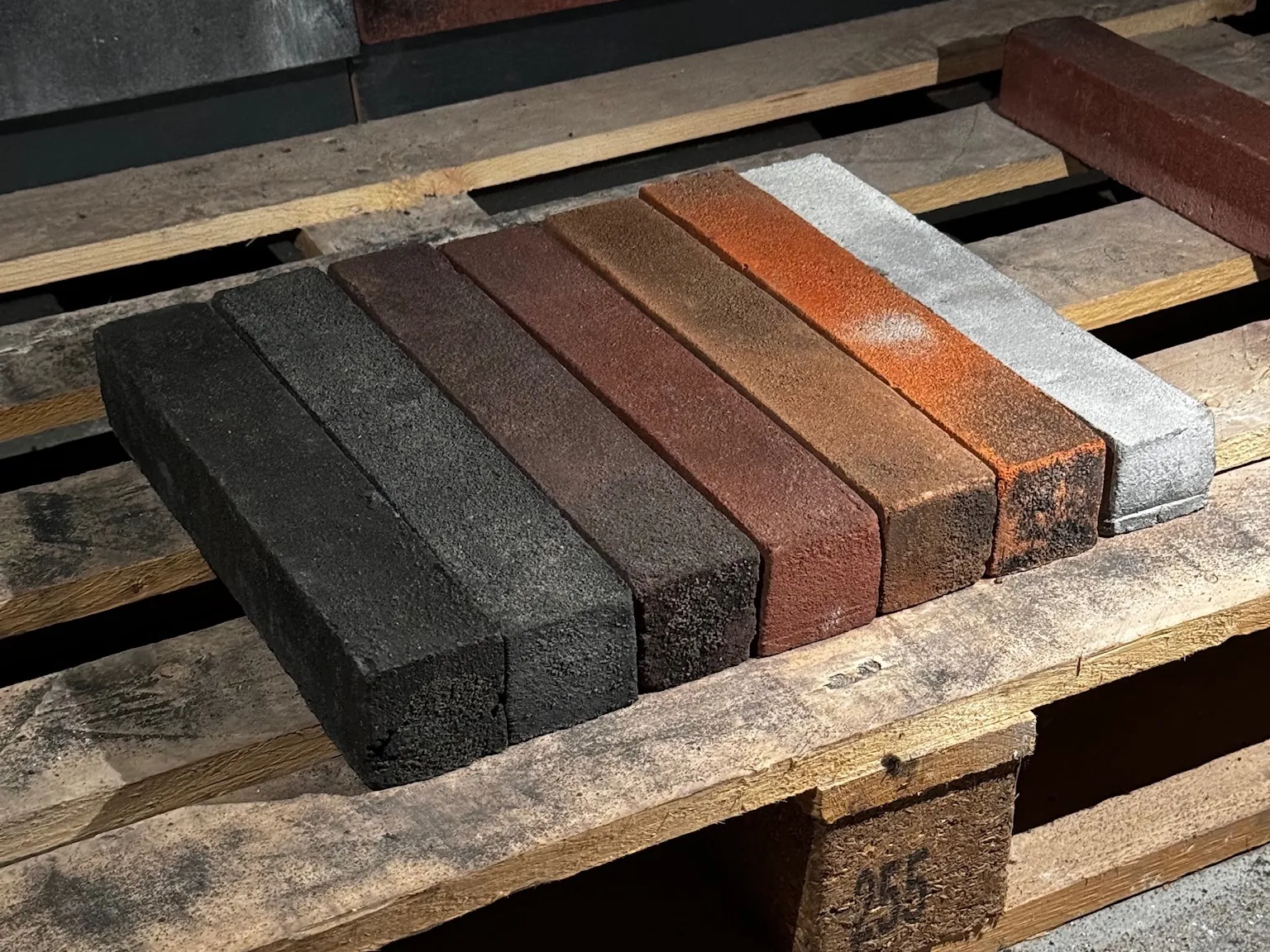 Сім виробів GoodBrick ручної формовки різних кольорів на дерев'яній палеті, видно торці й товщину